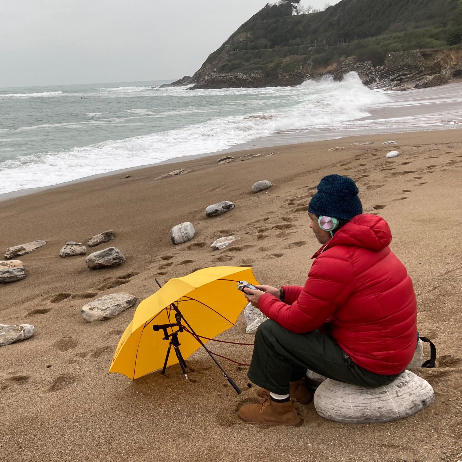 Brice Salek of Ringtone Records 26 making a field recording on a beach beside a yellow umbrella.